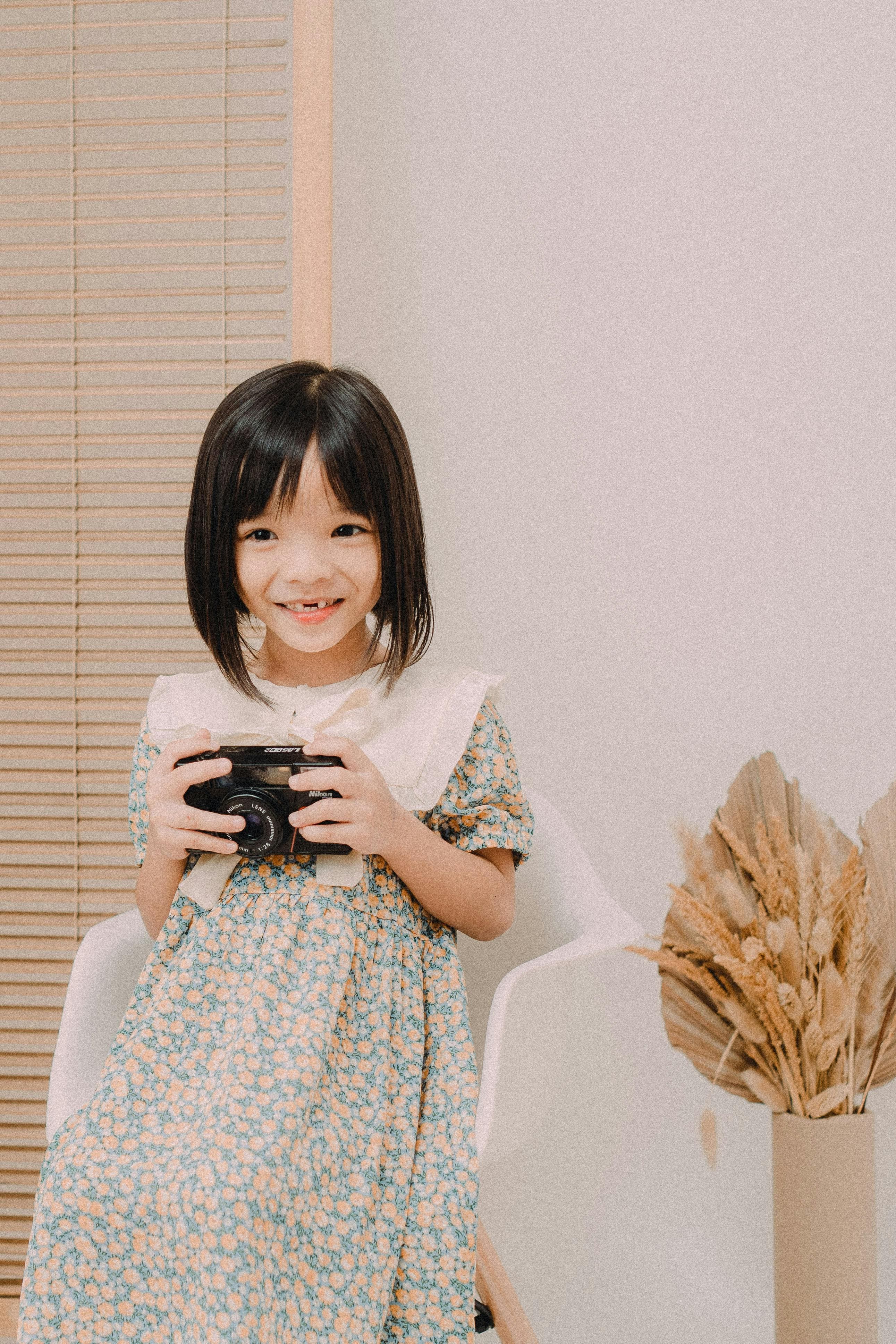 Young child in a floral dress holding a camera